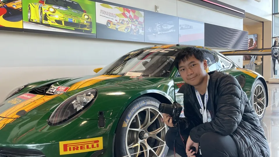 Porsche Chang crouching beside a green race car, holding a camera